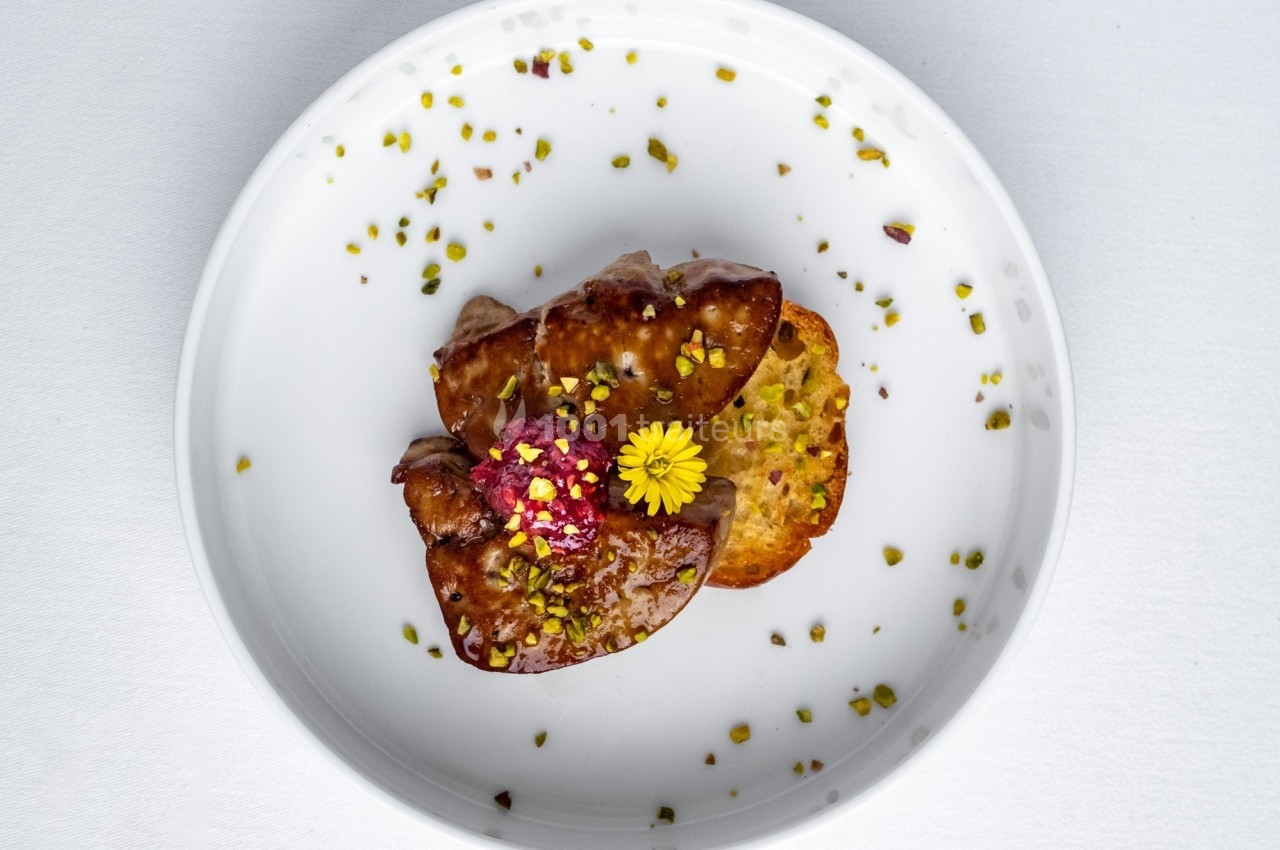 Assiette contenant une tranche de foie gras, une fleur comestible, une confiture rouge et des éclats de pistache.