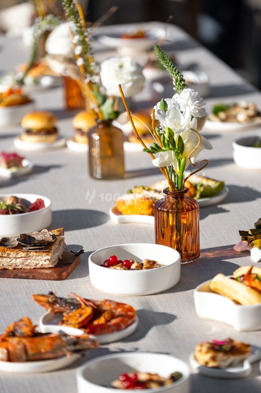 Table dressée avec divers plats et amuse-bouches, accompagnés de fleurs blanches dans des vases en verre ambré.