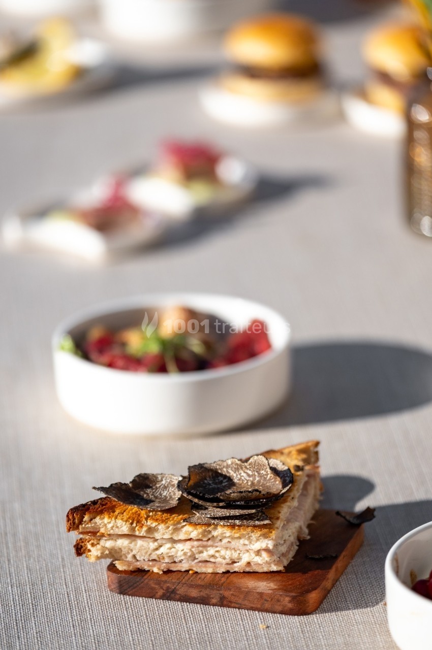 Tranche de pain grillé garnie de truffes noires, posée sur une planche en bois, avec des plats flous en arrière-plan.