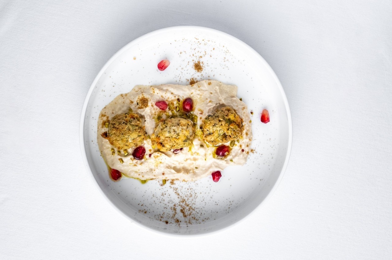 Assiette contenant trois falafels sur un lit de sauce blanche, garnis de graines de grenade et d'épices.