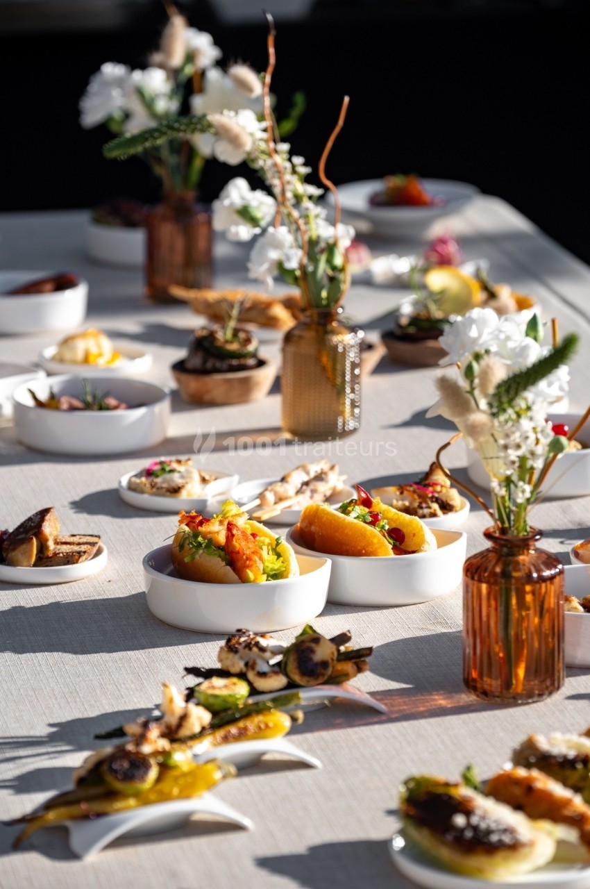 Table dressée avec des assiettes de tapas variées et des vases contenant des fleurs blanches et feuillages.