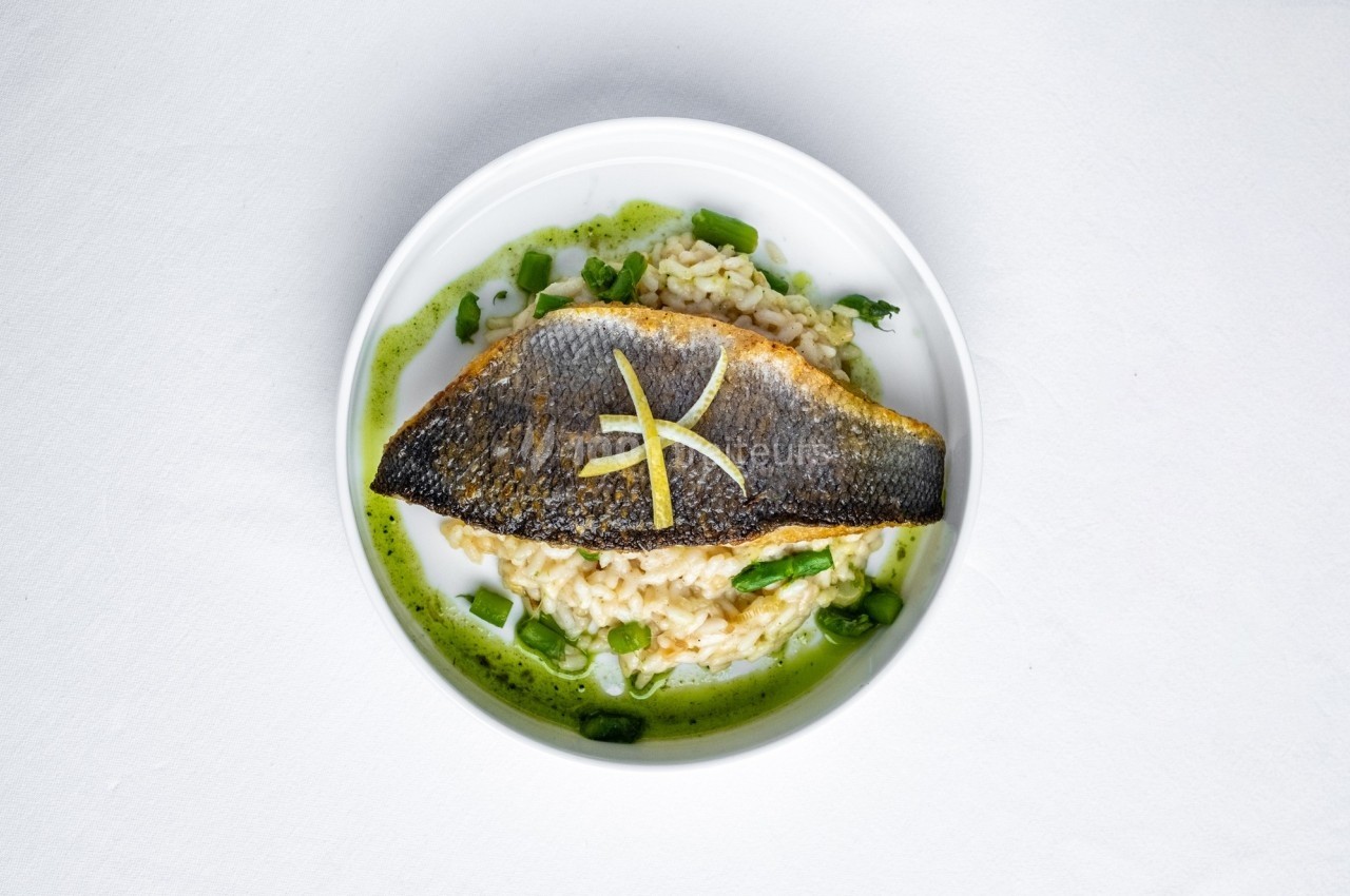 Filet de poisson grillé sur un risotto crémeux, accompagné d'asperges et d'une sauce verte.