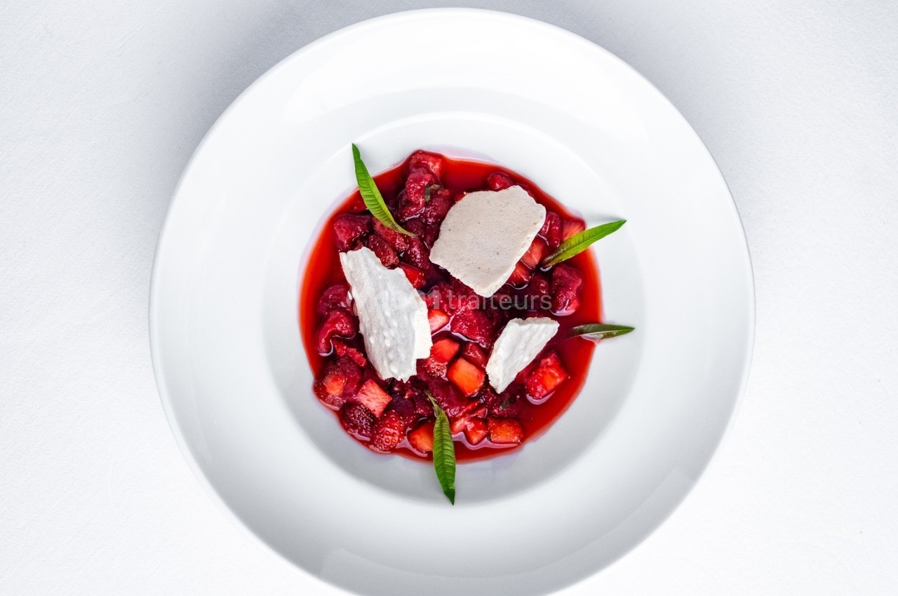 Assiette blanche contenant un dessert composé de fruits rouges, morceaux de meringue et feuilles décoratives.