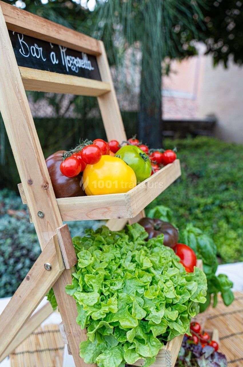 Stand en bois avec des légumes frais, incluant tomates, poivrons et laitue, exposé en extérieur près de végétation.