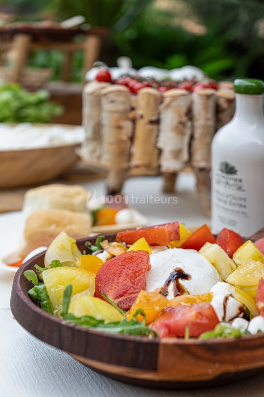 Salade colorée avec tomates, mozzarella, roquette et filet de vinaigre balsamique, présentée dans un bol en bois.