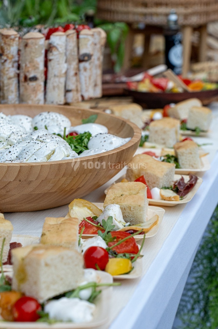Buffet avec salade de mozzarella, focaccia, légumes frais et autres plats disposés sur une table blanche.