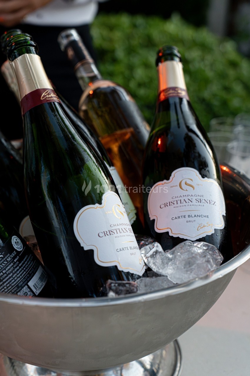 Bouteille de champagne dans un seau rempli de glace, entourée d'autres bouteilles et d'un arrière-plan flou.