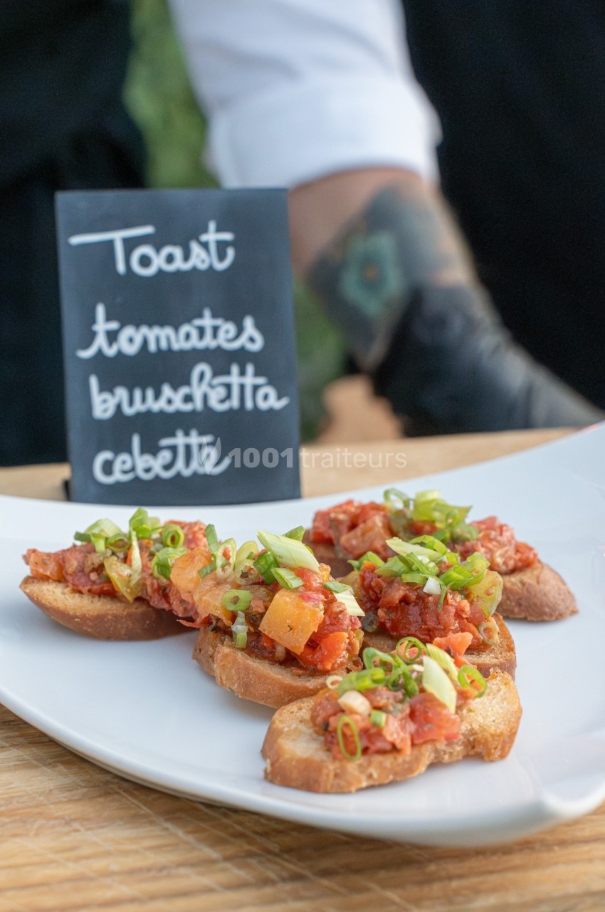 Toasts garnis de tomates, cébettes et herbes fraîches, présentés sur une assiette blanche avec une ardoise descriptive.