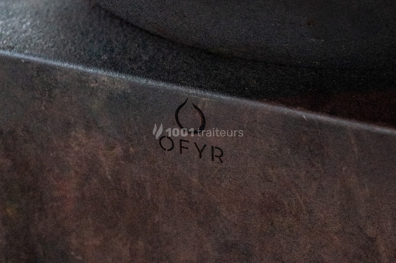 Logo ’OFYR’ gravé sur une surface métallique sombre avec une texture brute.