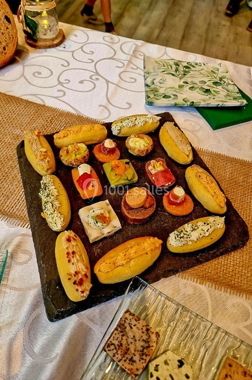 Plateau d'amuse-bouches variés disposés sur une ardoise, entouré de décorations de table en tissu et en bois.