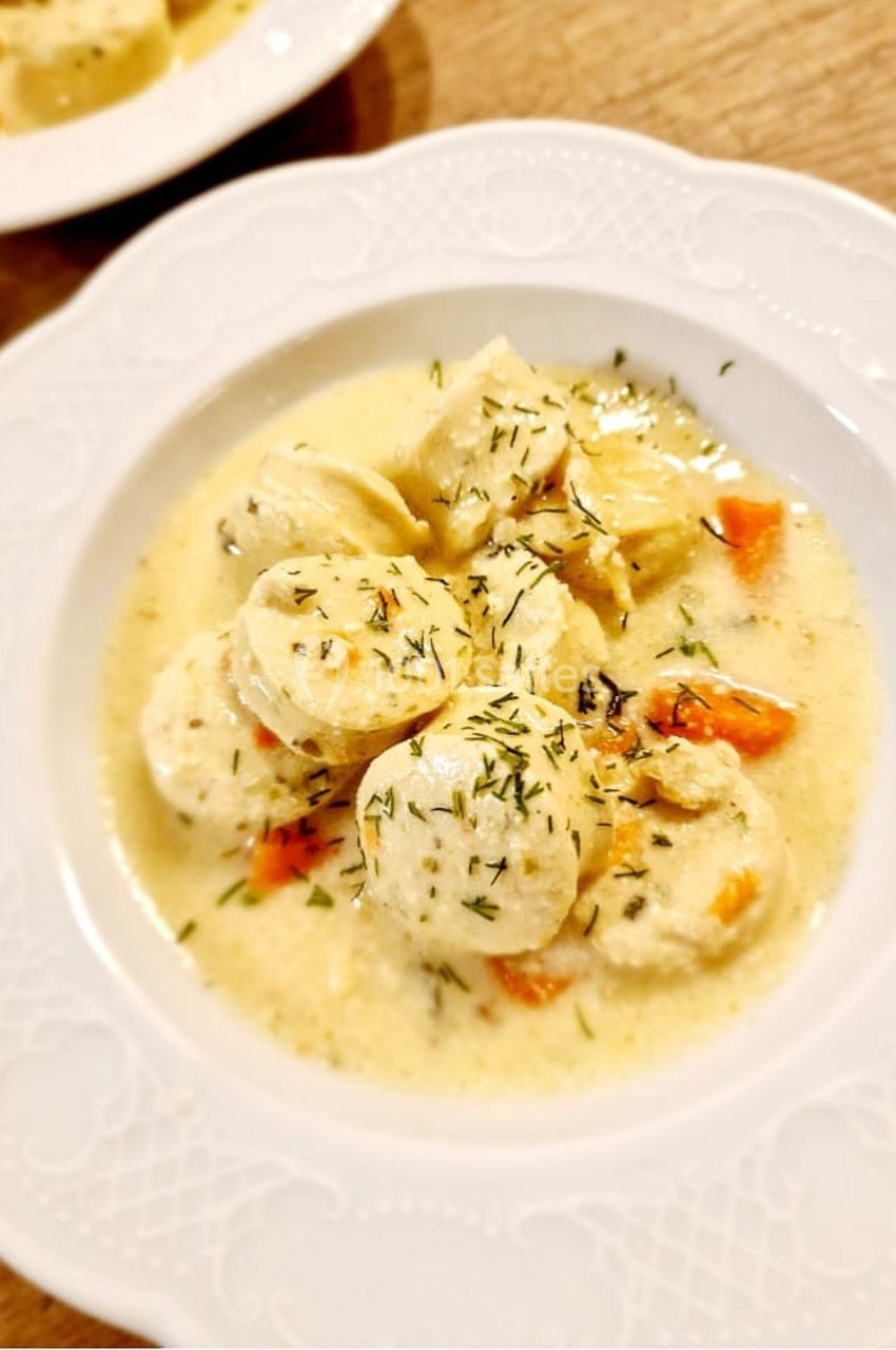 Assiette de quenelles servies dans une sauce crémeuse avec des morceaux de carottes et des herbes.