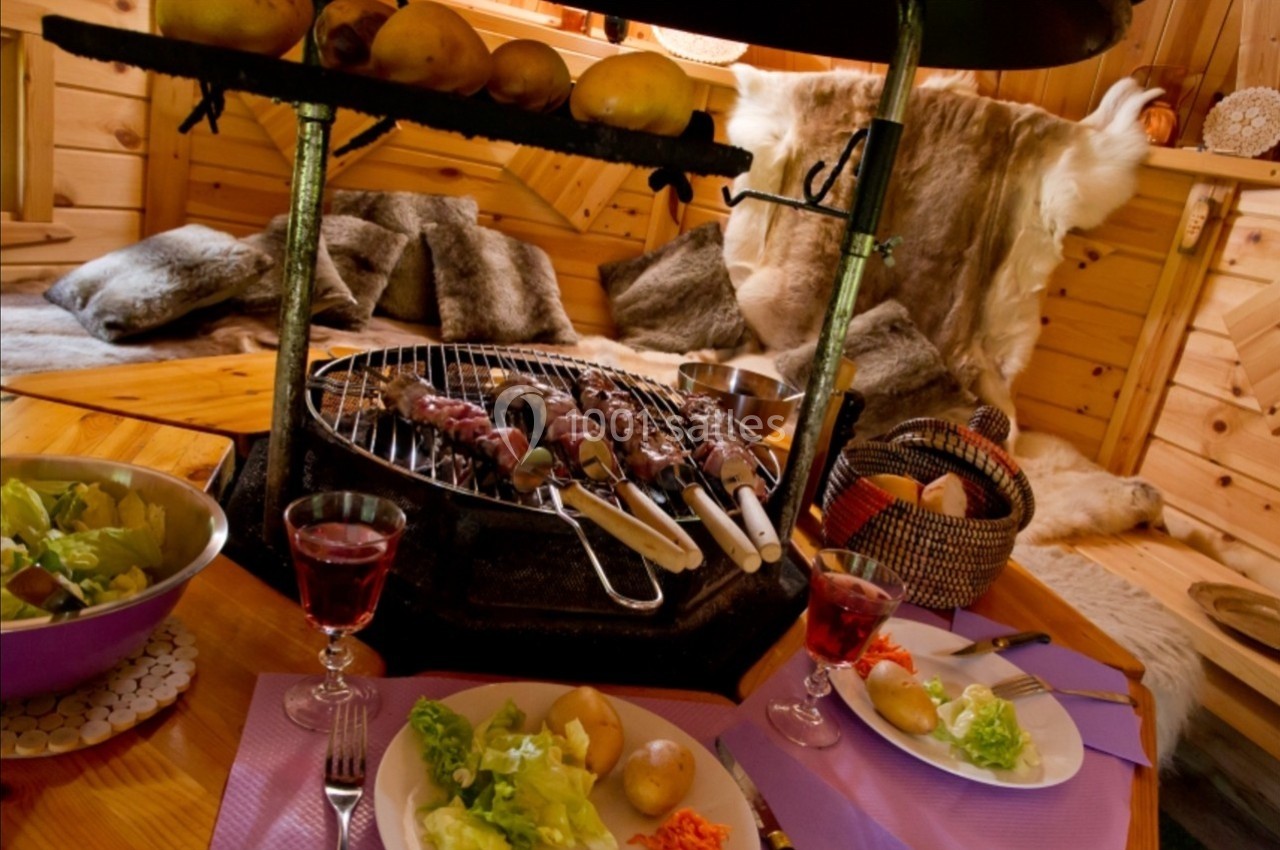 Repas convivial avec brochettes grillées, salades et vin rouge, dans un intérieur en bois au décor chaleureux.