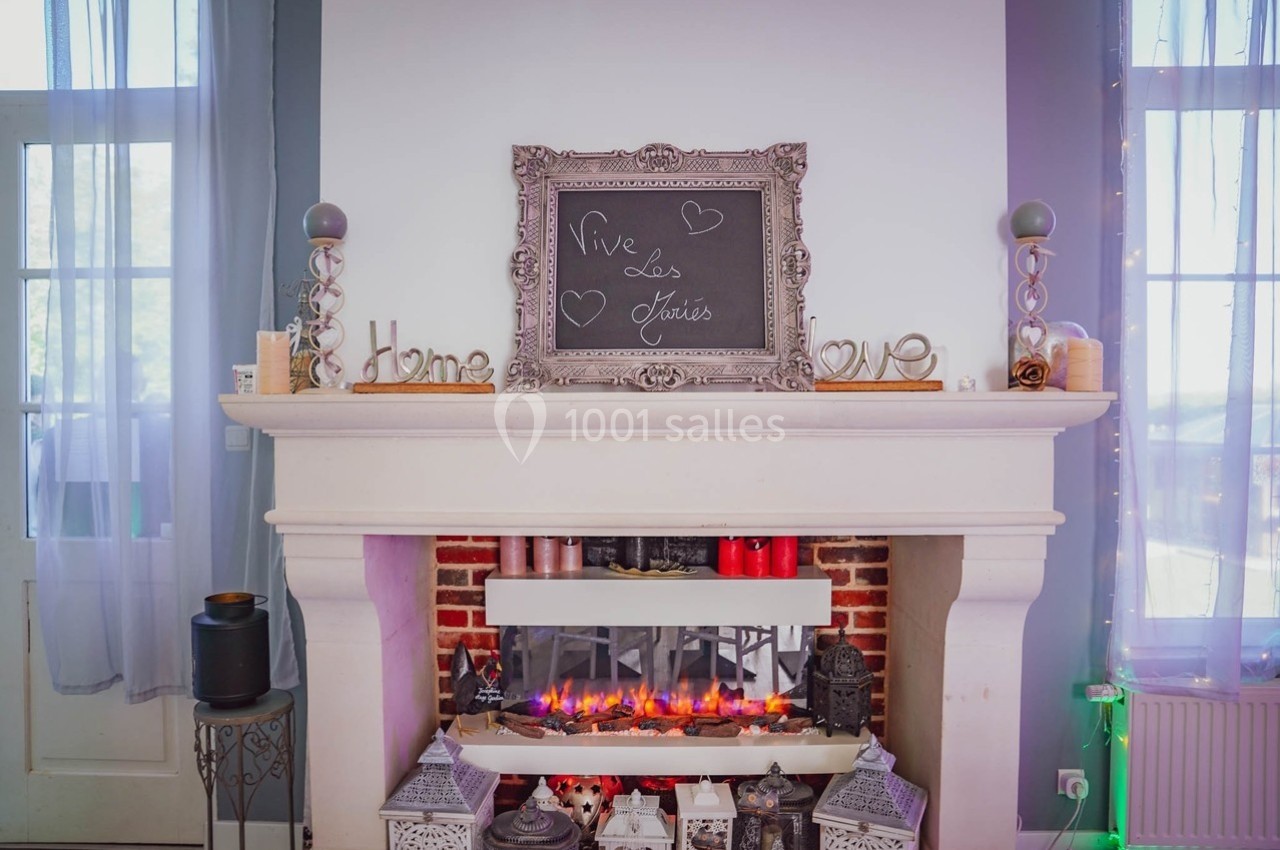 Cheminée décorative avec bougies, lanternes et tableau noir inscrit ’Vive les mariés’, dans un intérieur lumineux.