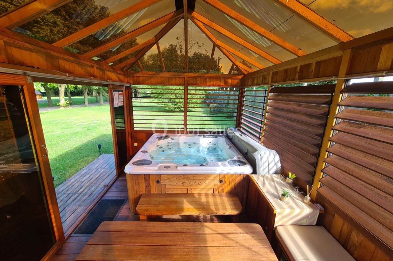 Abri en bois avec un jacuzzi intégré, entouré de grandes ouvertures donnant sur un jardin verdoyant.