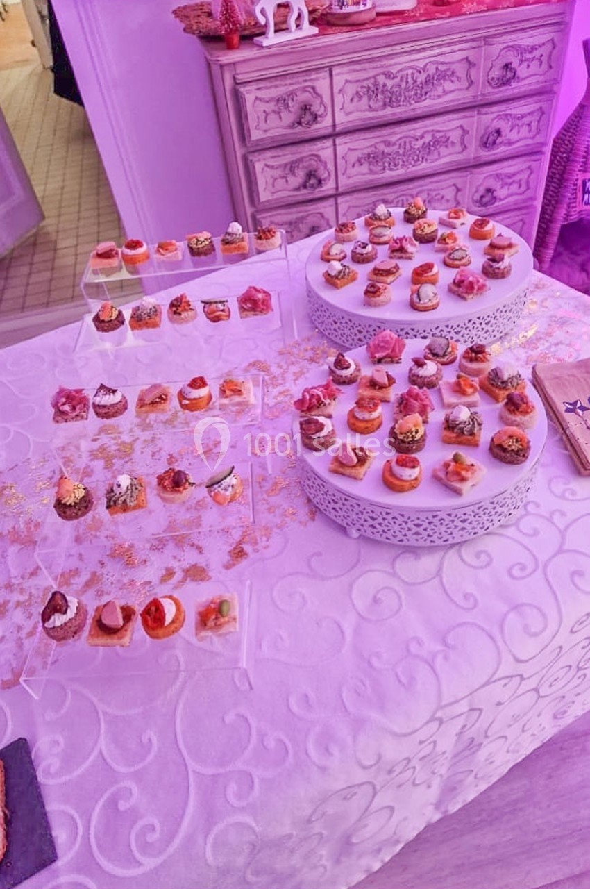 Plateau de canapés variés disposés sur une table blanche décorée, dans un environnement éclairé en lumière violette.