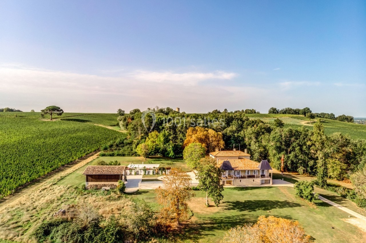 Vue aérienne d'une maison entourée de champs, d'arbres et d'un espace extérieur aménagé avec piscine.