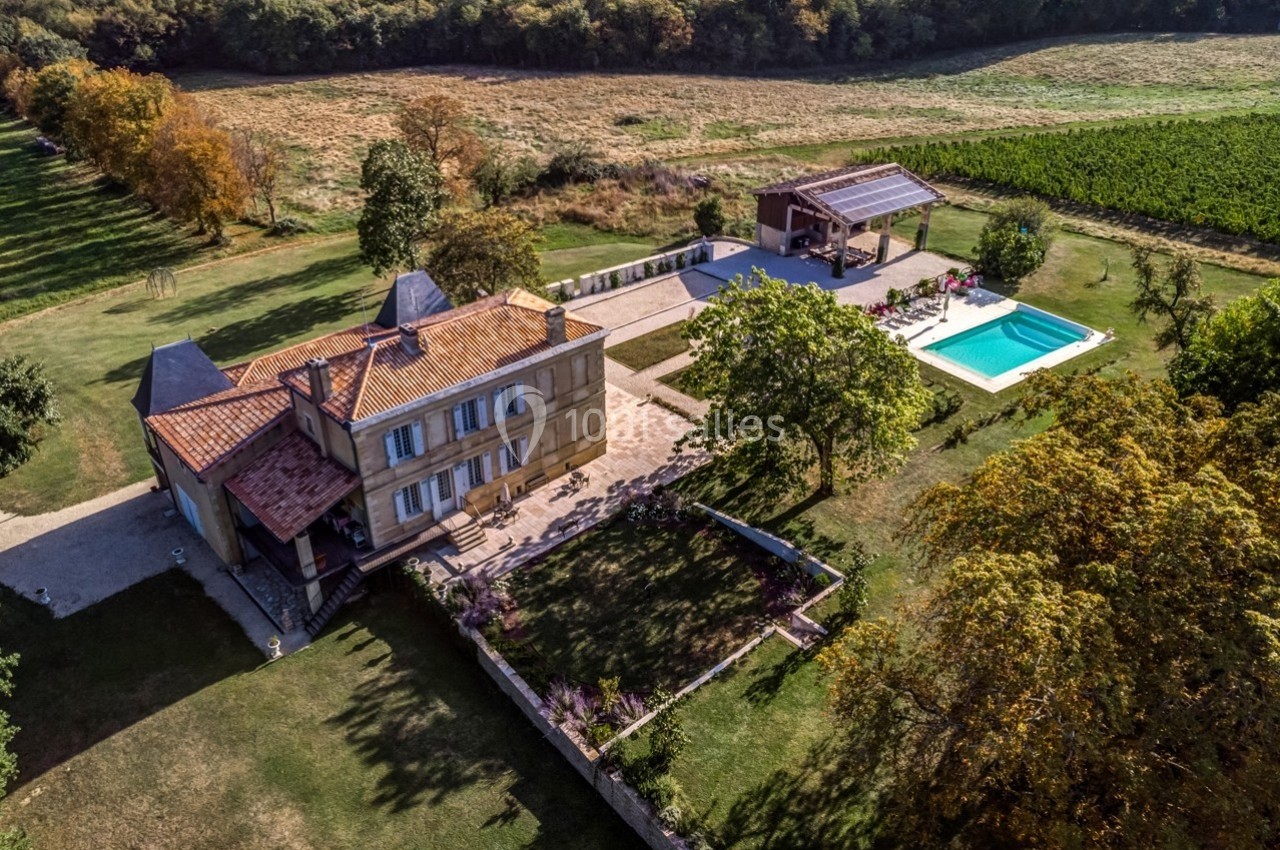 Vue aérienne d'une maison en pierre avec piscine, terrasse et jardin, entourée de champs et d'arbres.