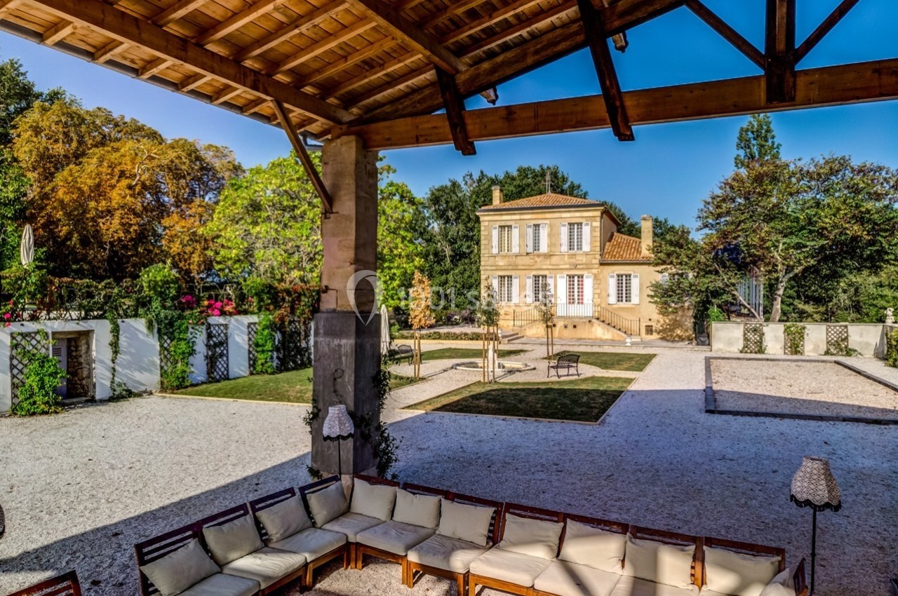 Vue d'une maison provençale entourée de jardins, prise depuis une terrasse couverte avec des sièges en bois.