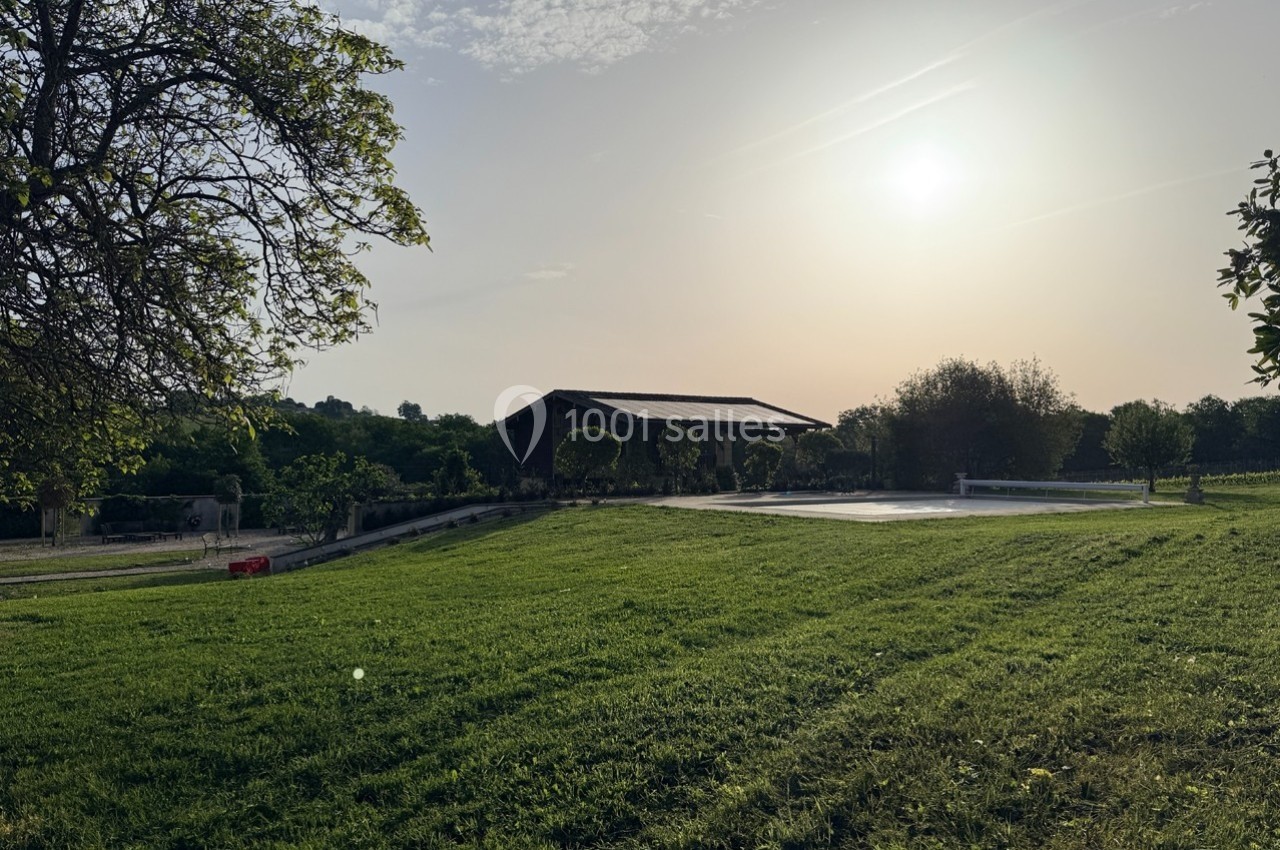 Pelouse verdoyante au coucher du soleil avec une piscine couverte et un bâtiment en arrière-plan.