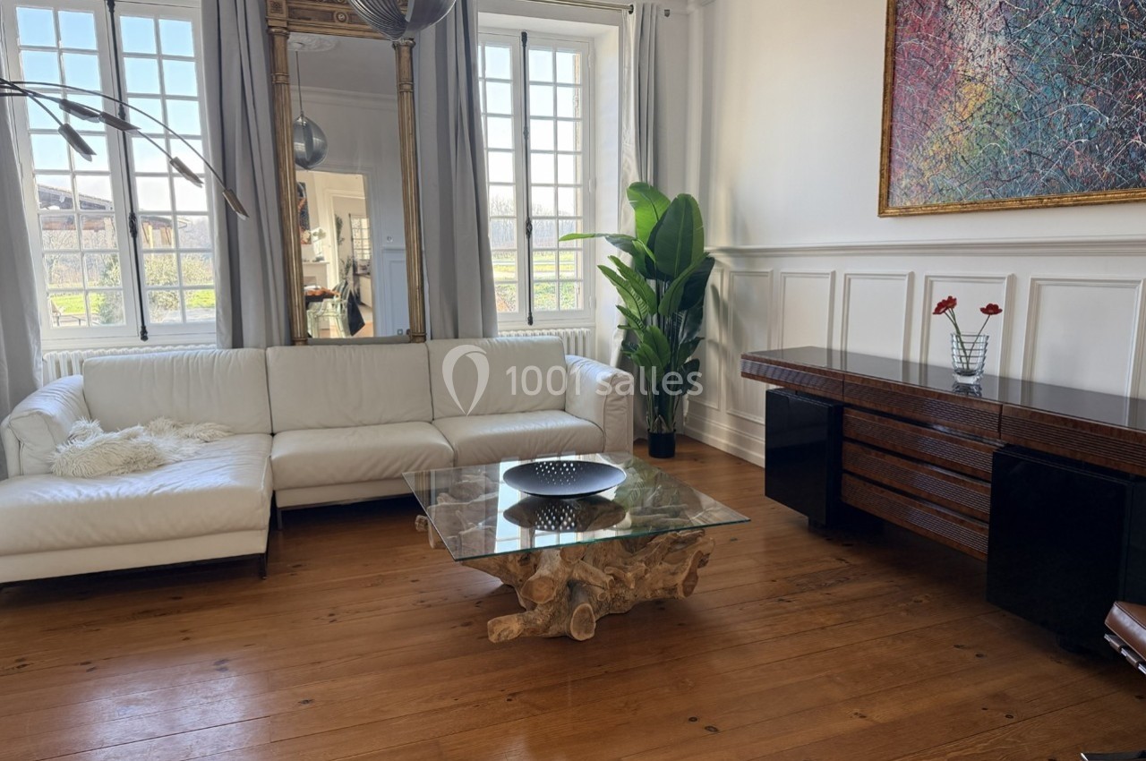 Salon lumineux avec canapé blanc, table basse en verre, plante verte, tableau coloré et parquet en bois.