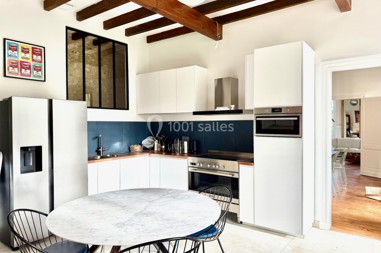 Cuisine moderne avec table ronde en marbre, électroménagers en acier inoxydable et poutres apparentes au plafond.
