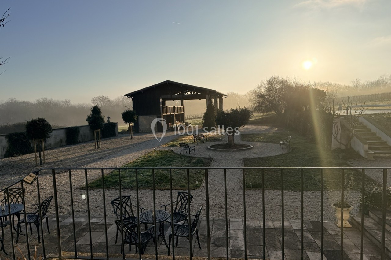 Cour extérieure avec mobilier de jardin, vue sur un bâtiment ouvert et un paysage rural au lever du soleil.
