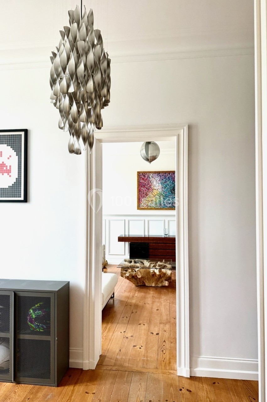 Vue d'un intérieur lumineux avec un lustre design, un parquet en bois clair et des œuvres d'art accrochées aux murs.