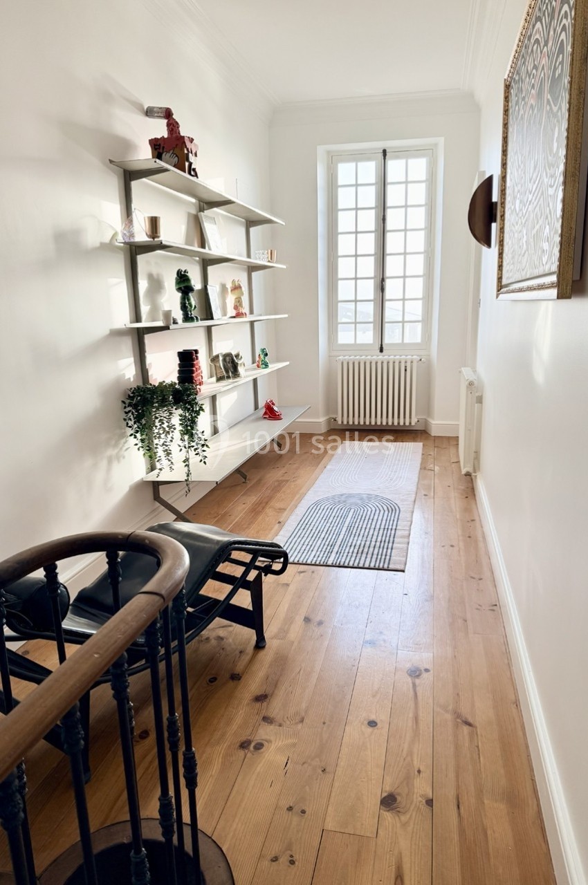 Couloir lumineux avec parquet en bois, étagères décoratives, chaise longue et fenêtre laissant entrer la lumière naturelle.