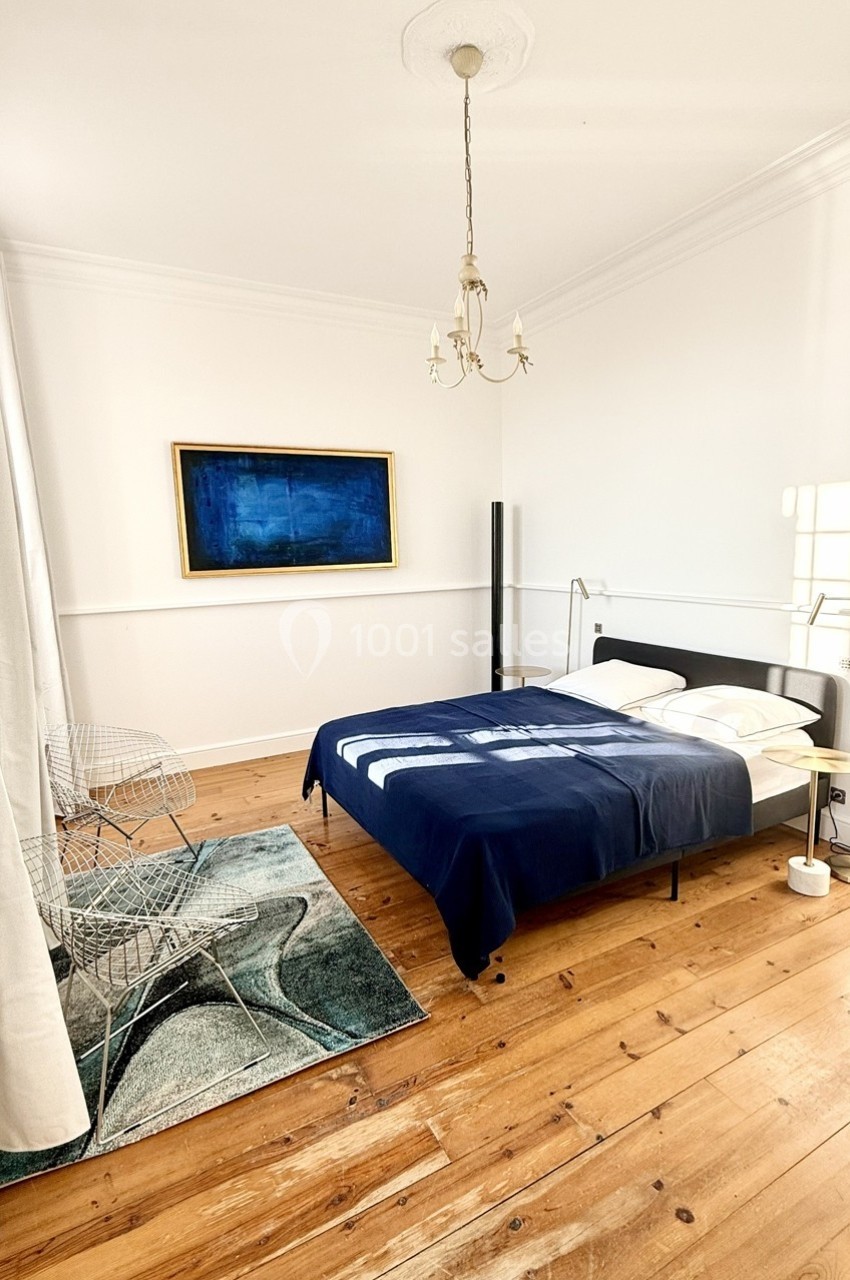 Chambre lumineuse avec parquet, lit double à couverture bleue, tableau abstrait et mobilier moderne.