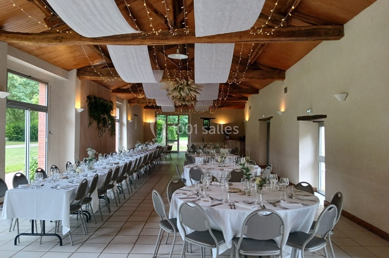 Salle de réception décorée avec des tables dressées, des guirlandes lumineuses et des voilages suspendus au plafond.