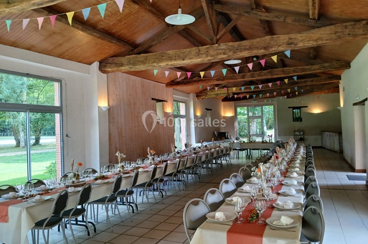 Salle de réception décorée avec des guirlandes colorées, tables dressées pour un repas festif avec vue sur l'extérieur.