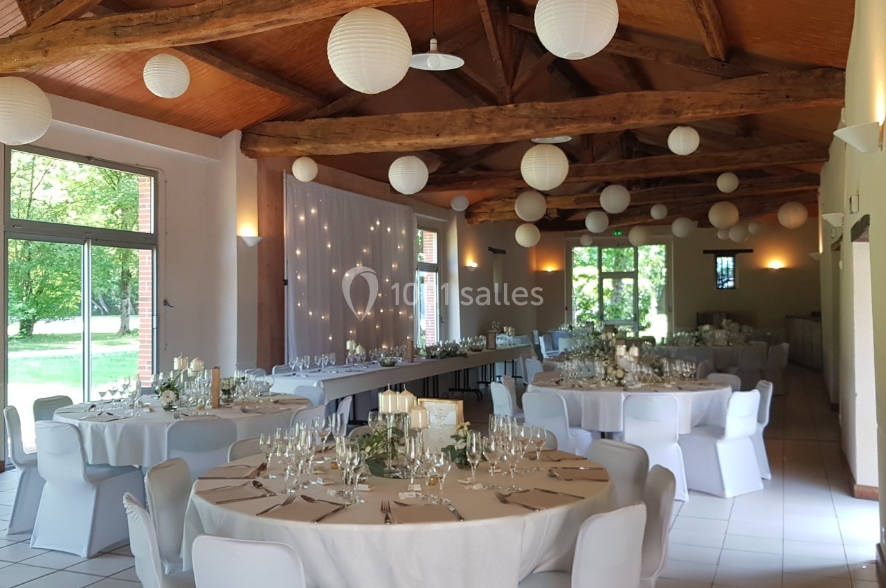 Salle de réception décorée avec des tables rondes dressées, des lanternes suspendues et des guirlandes lumineuses.