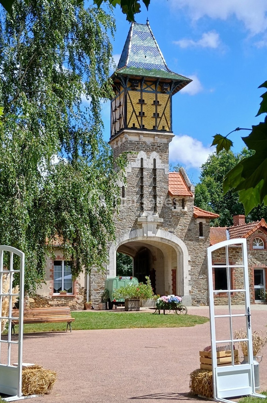 Tour en pierre avec toit en ardoise, entourée de verdure, vue à travers des portes ouvertes dans une cour pavée.
