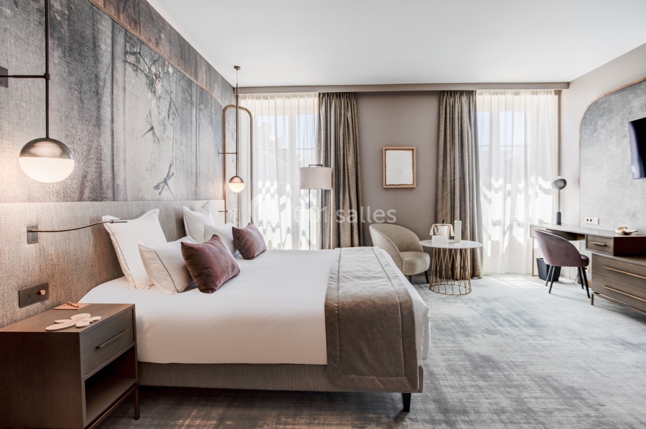 Chambre d'hôtel lumineuse avec un grand lit, des rideaux épais, un bureau, une télévision et une décoration moderne.