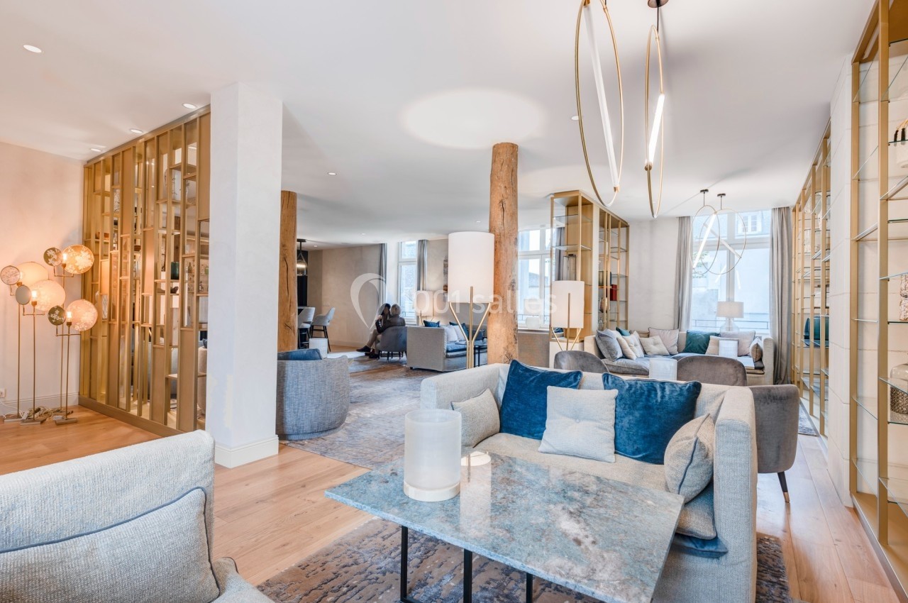 Espace intérieur lumineux avec mobilier moderne, canapés gris et bleus, tables en marbre et séparations dorées.