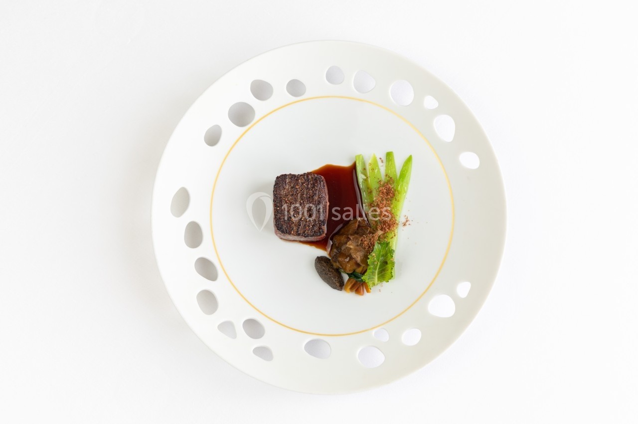 Assiette gastronomique avec un morceau de viande, sauce, légumes verts et morilles, présentée sur fond blanc.