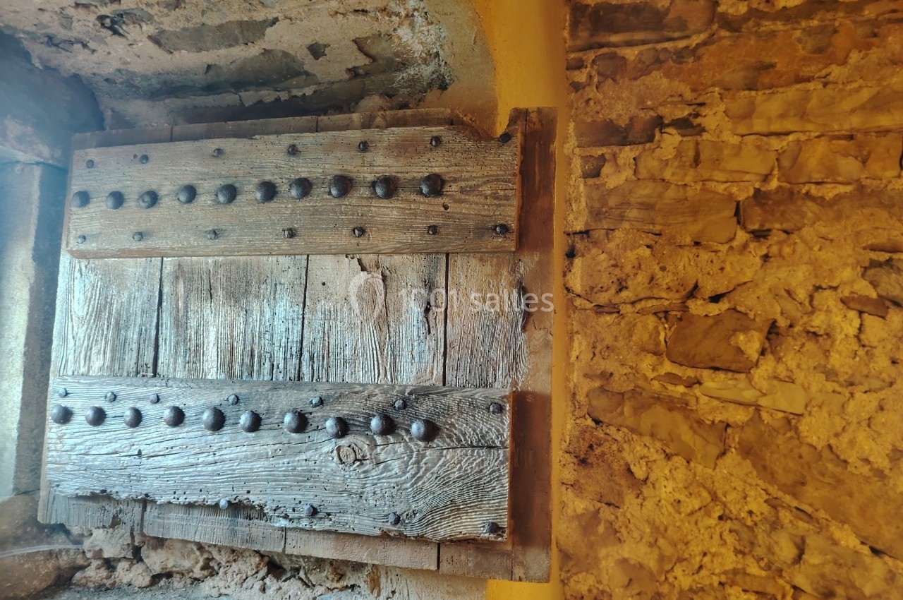 Porte en bois massif cloutée, encadrée par un mur en pierre ancienne et éclairée par une lumière chaude.