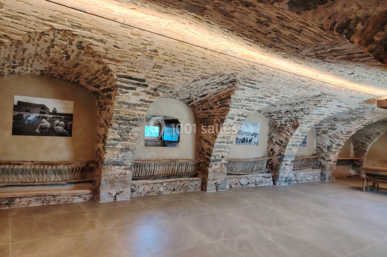 Salle voûtée en pierre avec bancs en bois, éclairage doux et photos accrochées aux murs.