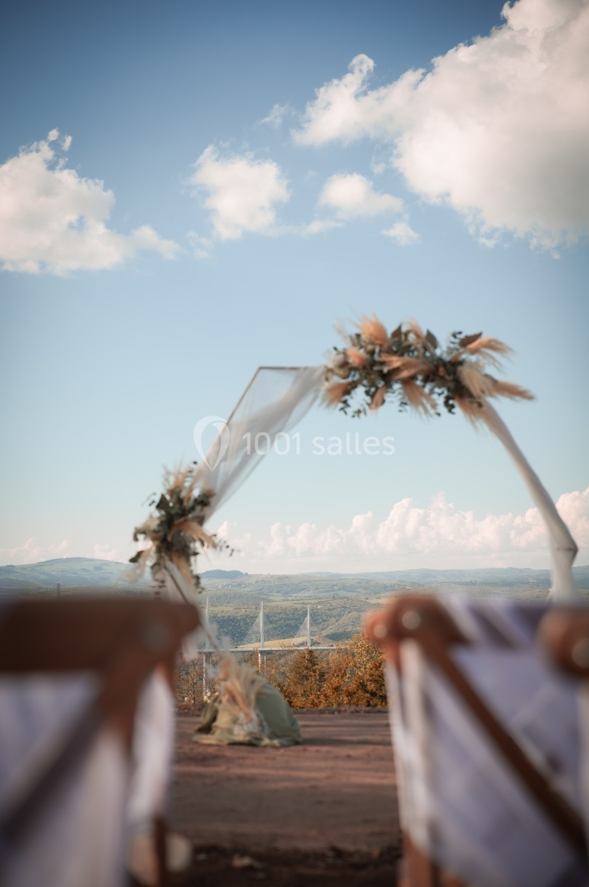 Arche de mariage décorée de fleurs séchées, installée en extérieur avec vue sur un paysage vallonné et un ciel dégagé.