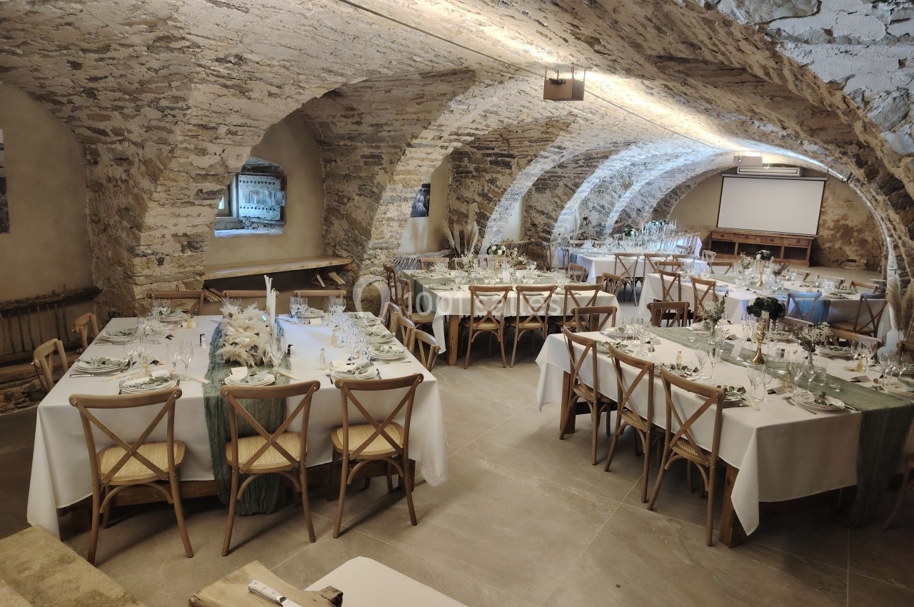 Salle voûtée en pierre aménagée pour un repas avec des tables dressées et décorées de manière élégante.