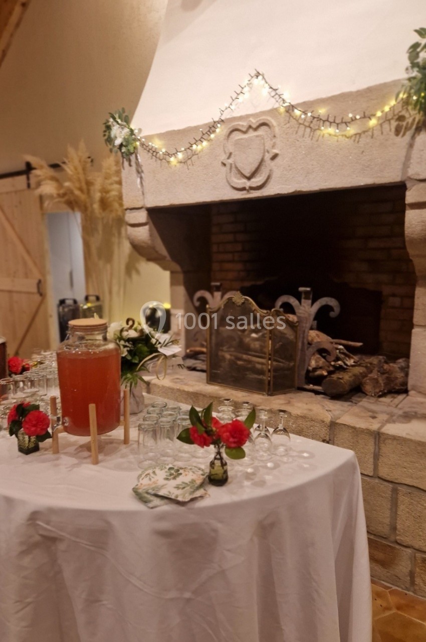 Table décorée avec boissons et fleurs devant une cheminée en pierre ornée de guirlandes lumineuses.