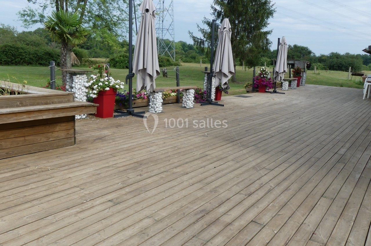 Terrasse en bois avec parasols fermés, jardinières fleuries et vue sur un jardin verdoyant en arrière-plan.