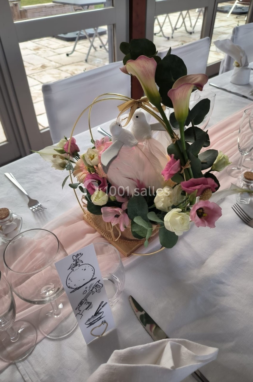 Centre de table floral avec des lys, des roses et une colombe décorative, disposé sur une nappe blanche.