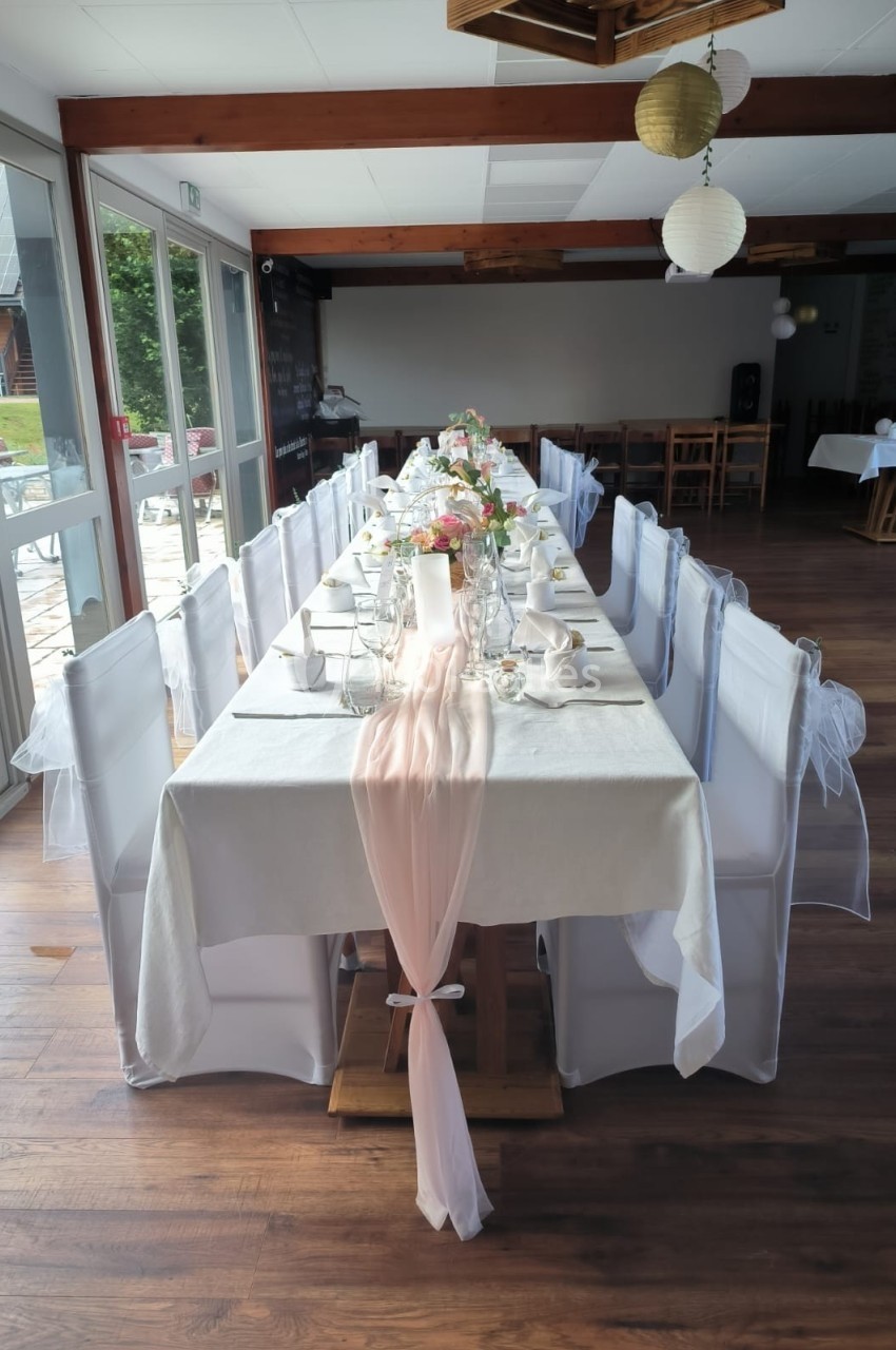 Table décorée pour un événement, nappée de blanc avec un chemin de table rose, fleurs et vaisselle élégante.