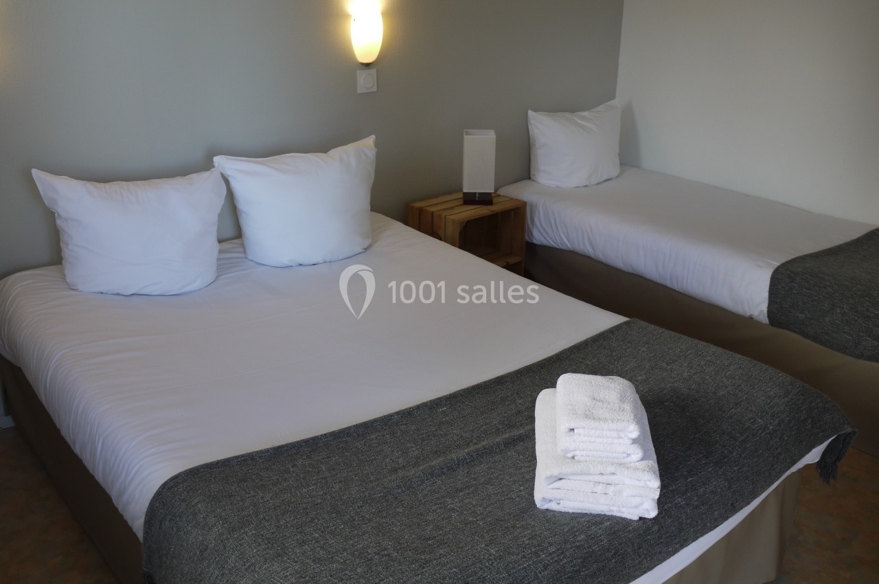 Deux lits simples avec draps blancs et couvertures grises dans une chambre éclairée par des appliques murales.