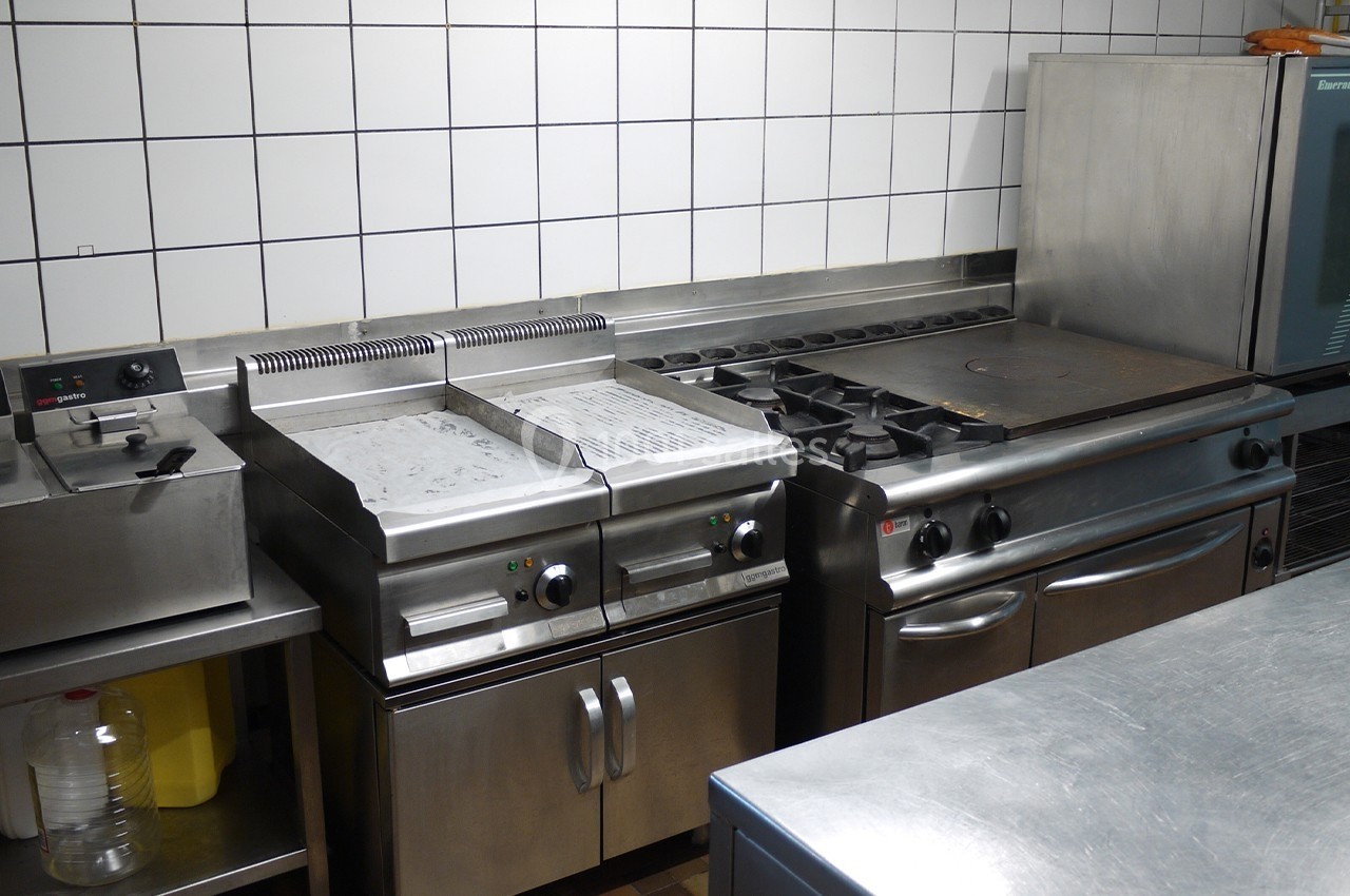 Cuisine professionnelle avec plaques de cuisson, friteuses et four, entourée de surfaces en acier inoxydable.