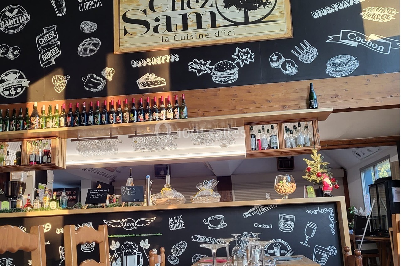 Intérieur d'un restaurant avec un bar en bois, des bouteilles alignées et un mur décoré de dessins et inscriptions à la…