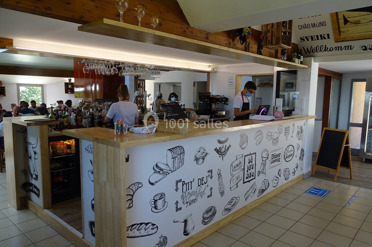 Un comptoir de bar en bois décoré de dessins alimentaires, avec des employés portant des masques et des clients en arrière…