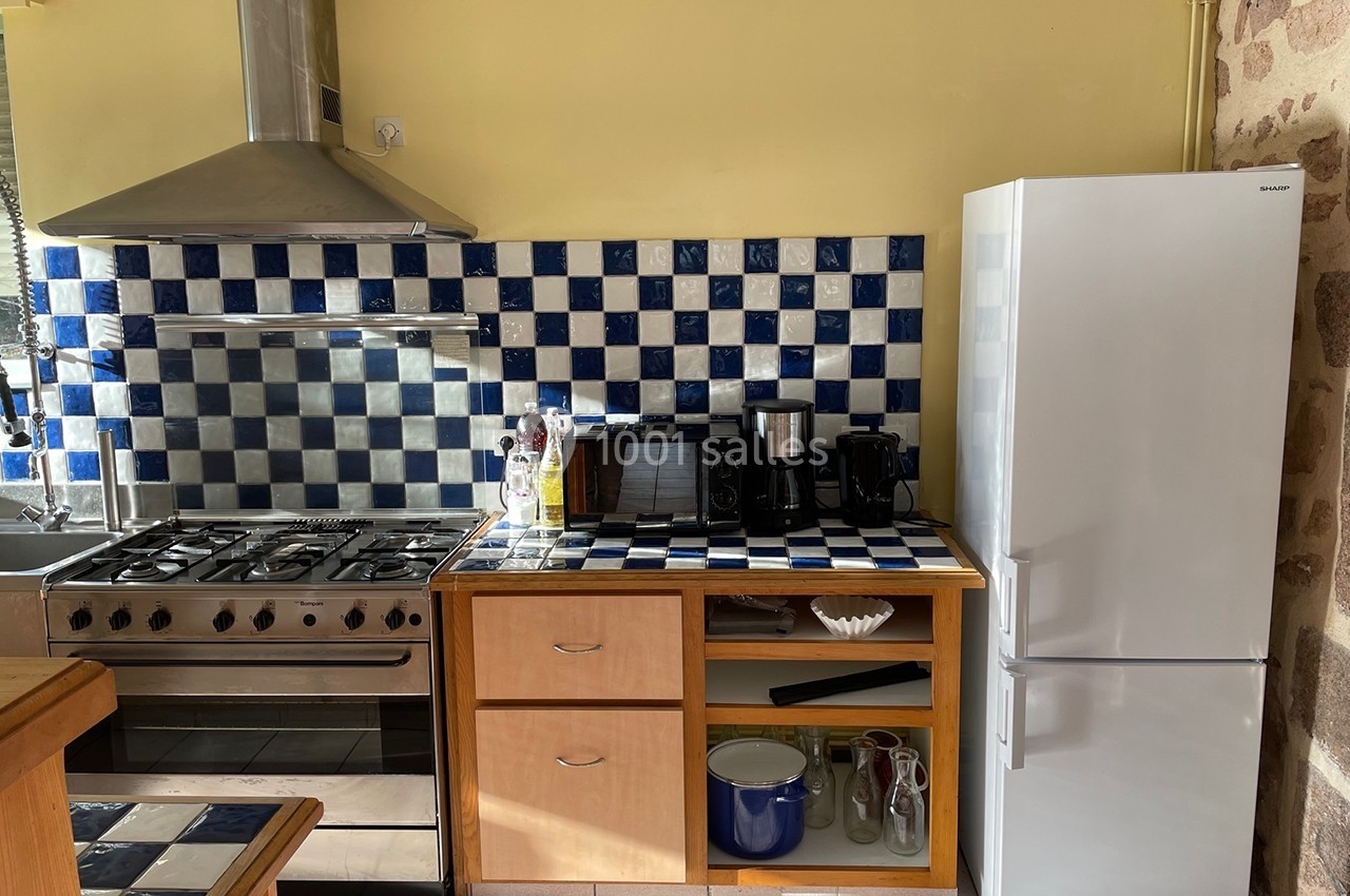 Cuisine équipée avec cuisinière à gaz, hotte, réfrigérateur blanc et plan de travail carrelé bleu et blanc.