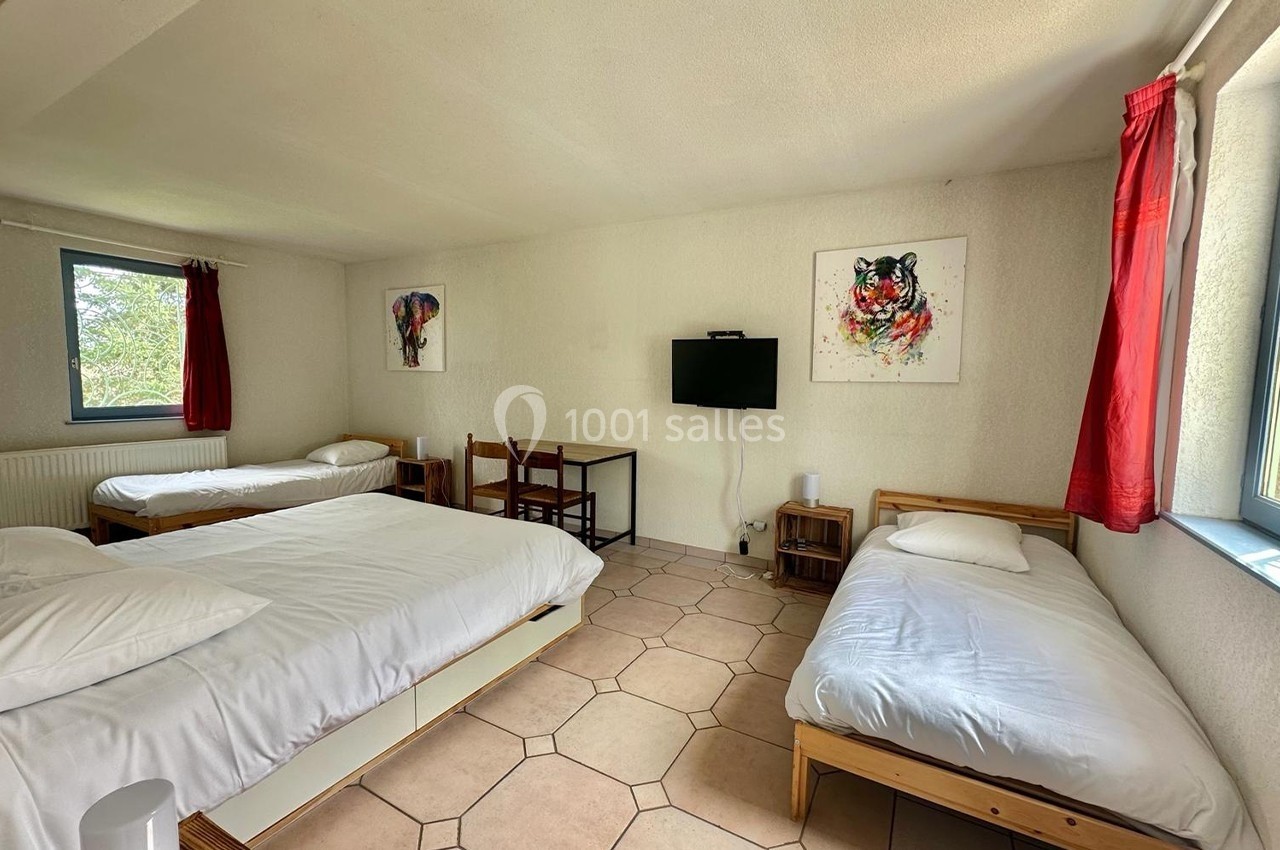 Chambre lumineuse avec trois lits, un bureau, une télévision murale et des tableaux colorés accrochés aux murs.